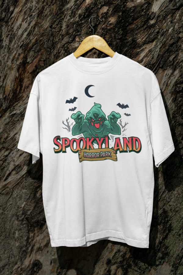 White Spookyland Horror Park T-shirt with a green ghost design hanging on a wooden hanger against a tree log background.