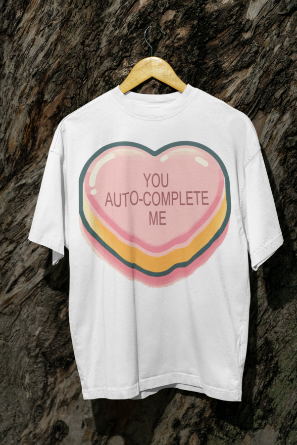 White T-shirt with a 'You Auto-Complete Me' heart design hanging on a wooden hanger.